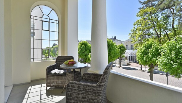 A balcony with wicker furniture, a table with fruit, and a view of trees and buildings. - Apartment near the beach 01 Villa Celia 6 pers. - Villa Celia Sellin (Sellin)