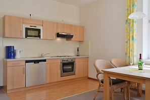 A compact kitchen with wooden cabinets, a built-in oven, and a dishwasher. There is a dining area with a table and chairs.