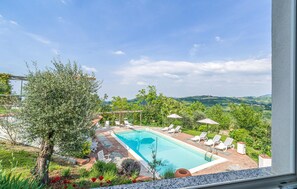 Una piscina rectangular con solárium empedrado, rodeada de sillas de descanso blancas y sombrillas.