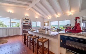 Una cocina con una isla grande, taburetes de bar, un horno Berkel rojo y vistas al campo.