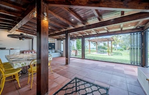 Un patio amplio con zona de comedor, techo de madera y vistas a un jardín y mobiliario de exterior.