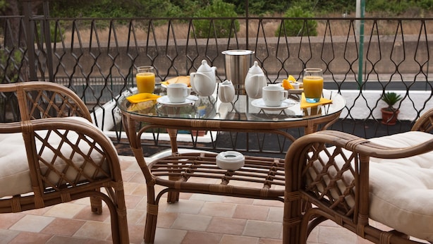 A breakfast setup on a glass table with wicker chairs, featuring a coffee pot, cups, a jug, and orange juice. - B&B Il Tempio di Hera (Castelvetrano)