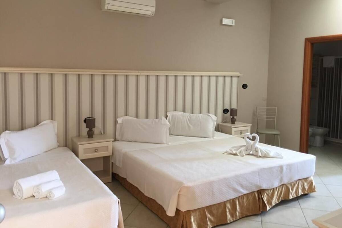 Habitación de hotel con dos camas, un ventanal grande, un radiador y un baño visible a través de una puerta abierta.