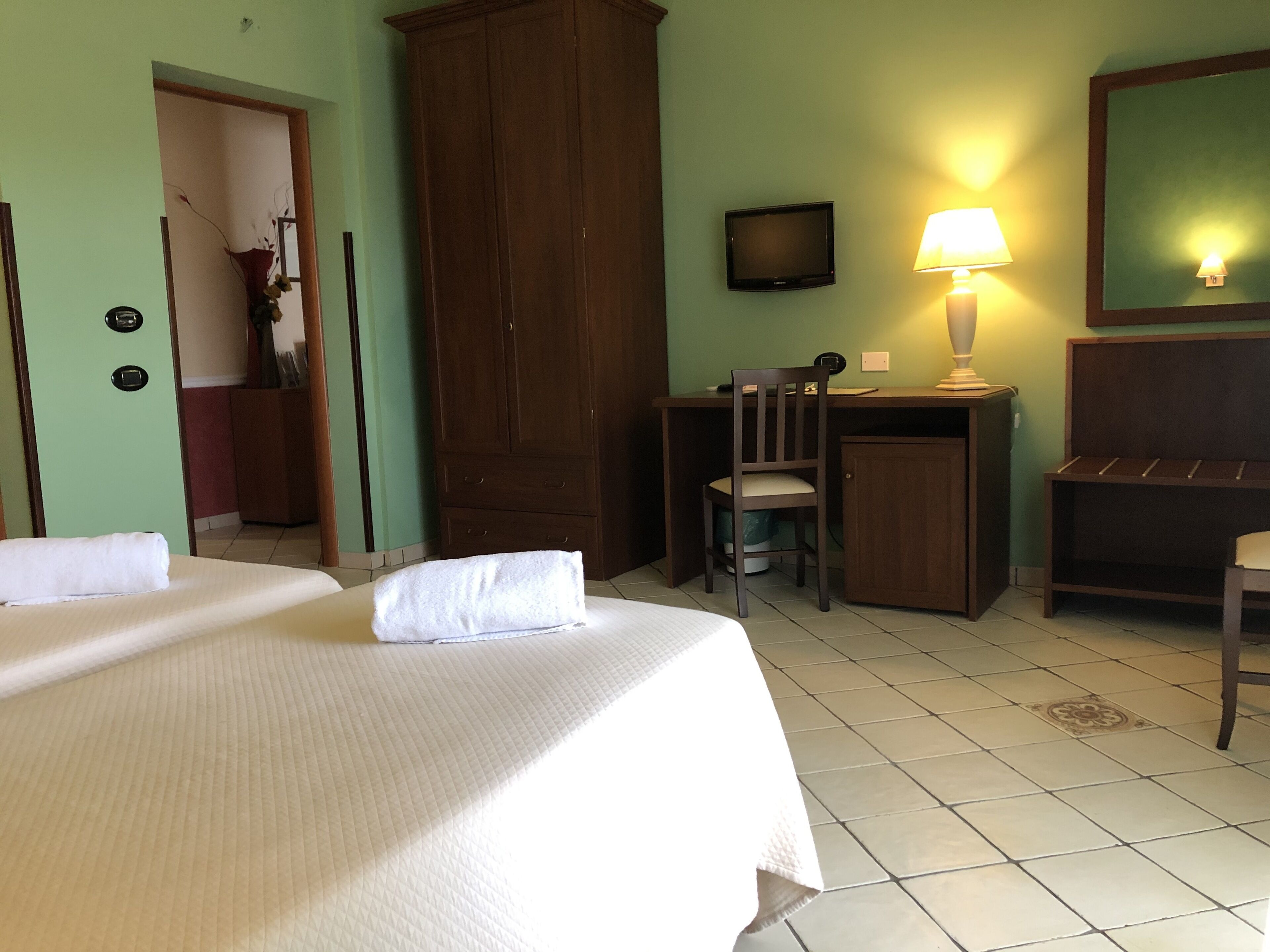 A hotel room with a bed, a desk with a chair, a television, and a lamp.