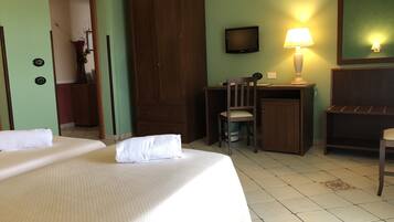 Quarto de hotel com cama, escrivaninha com cadeira, televisão e luminária.