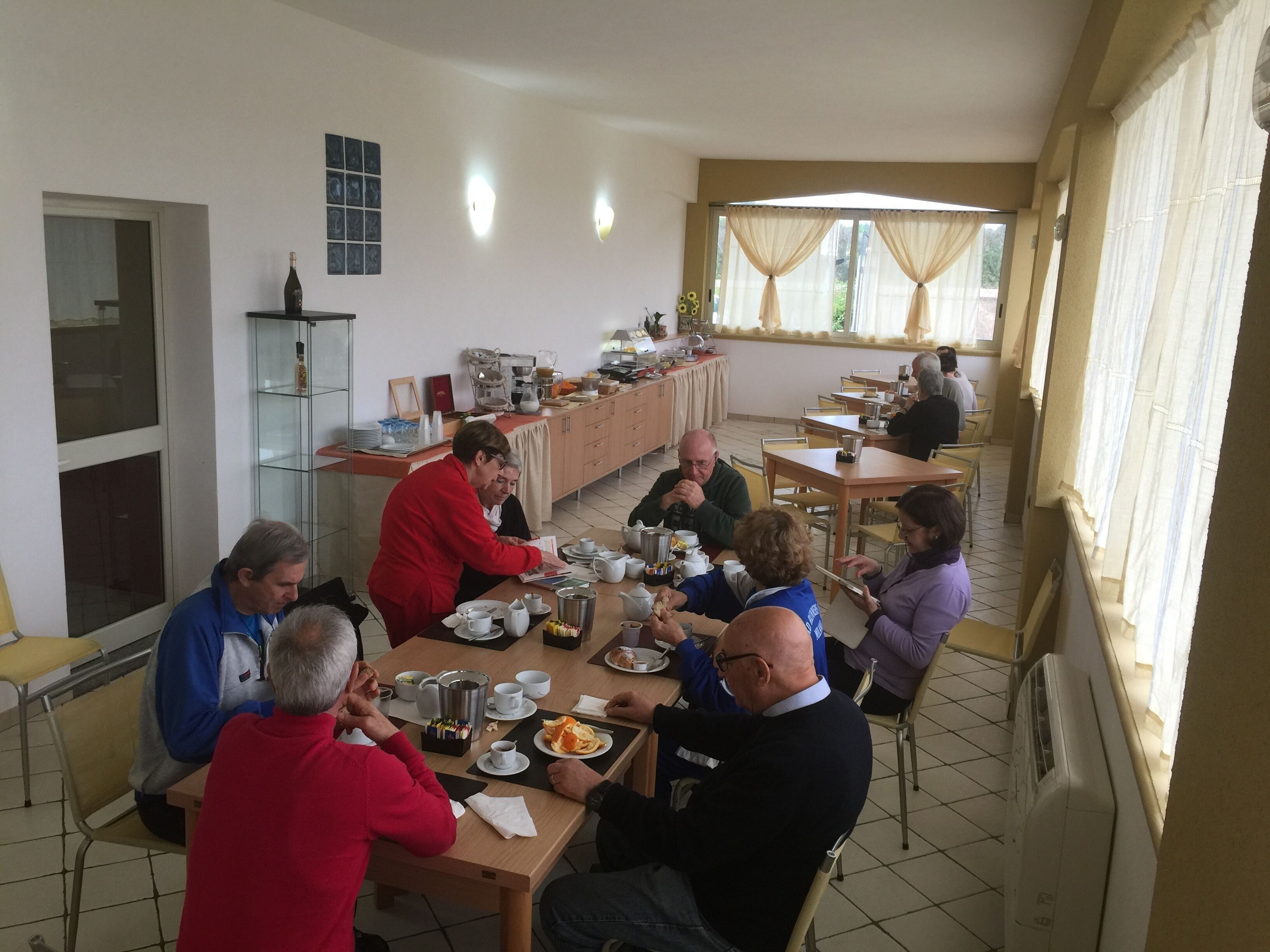 Un espace repas comprenant plusieurs tables et chaises, un buffet, et une fenêtre avec des rideaux.