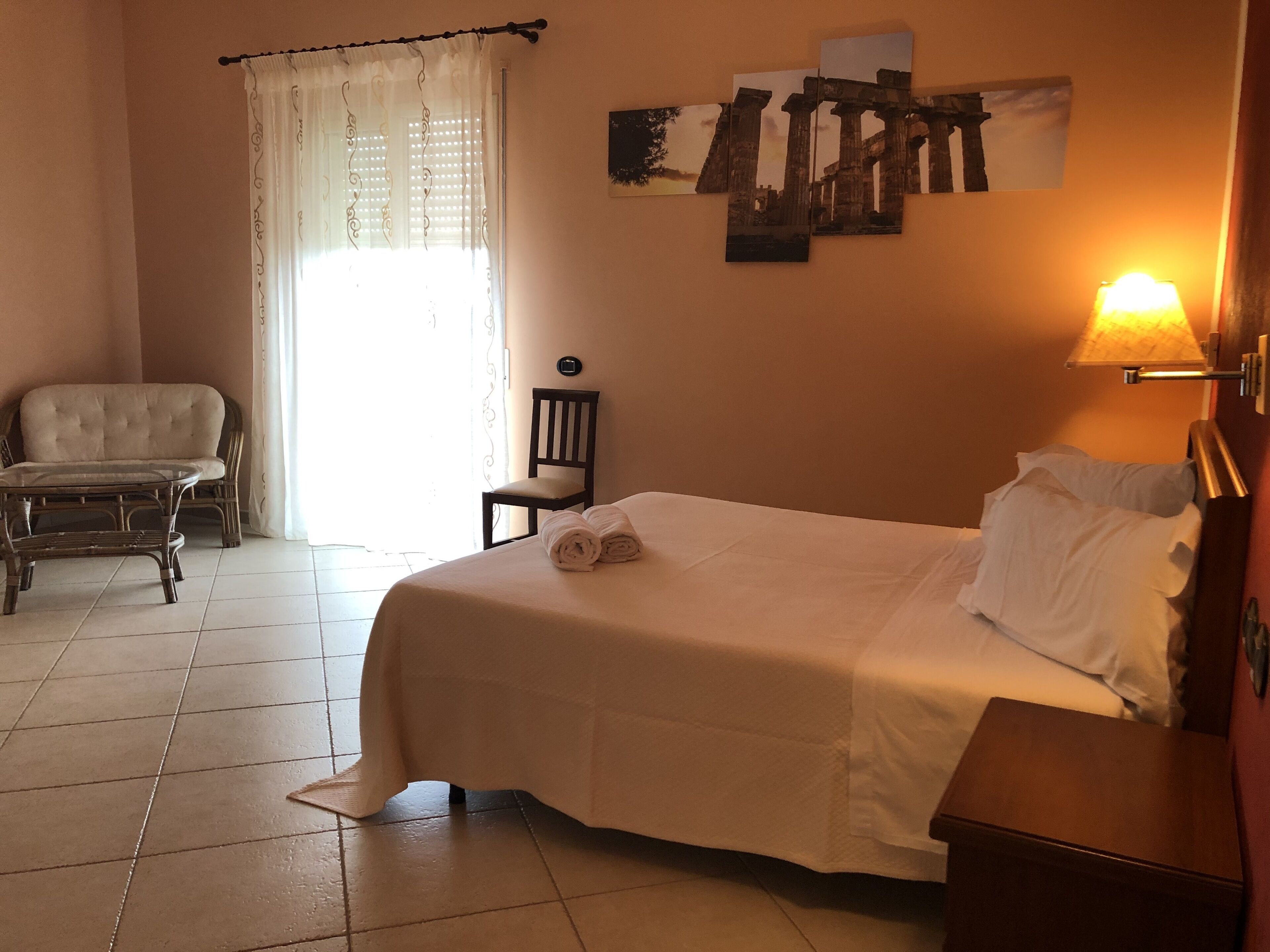 Una habitación de hotel con una cama, una silla, una mesita y una lámpara fijada a la pared.