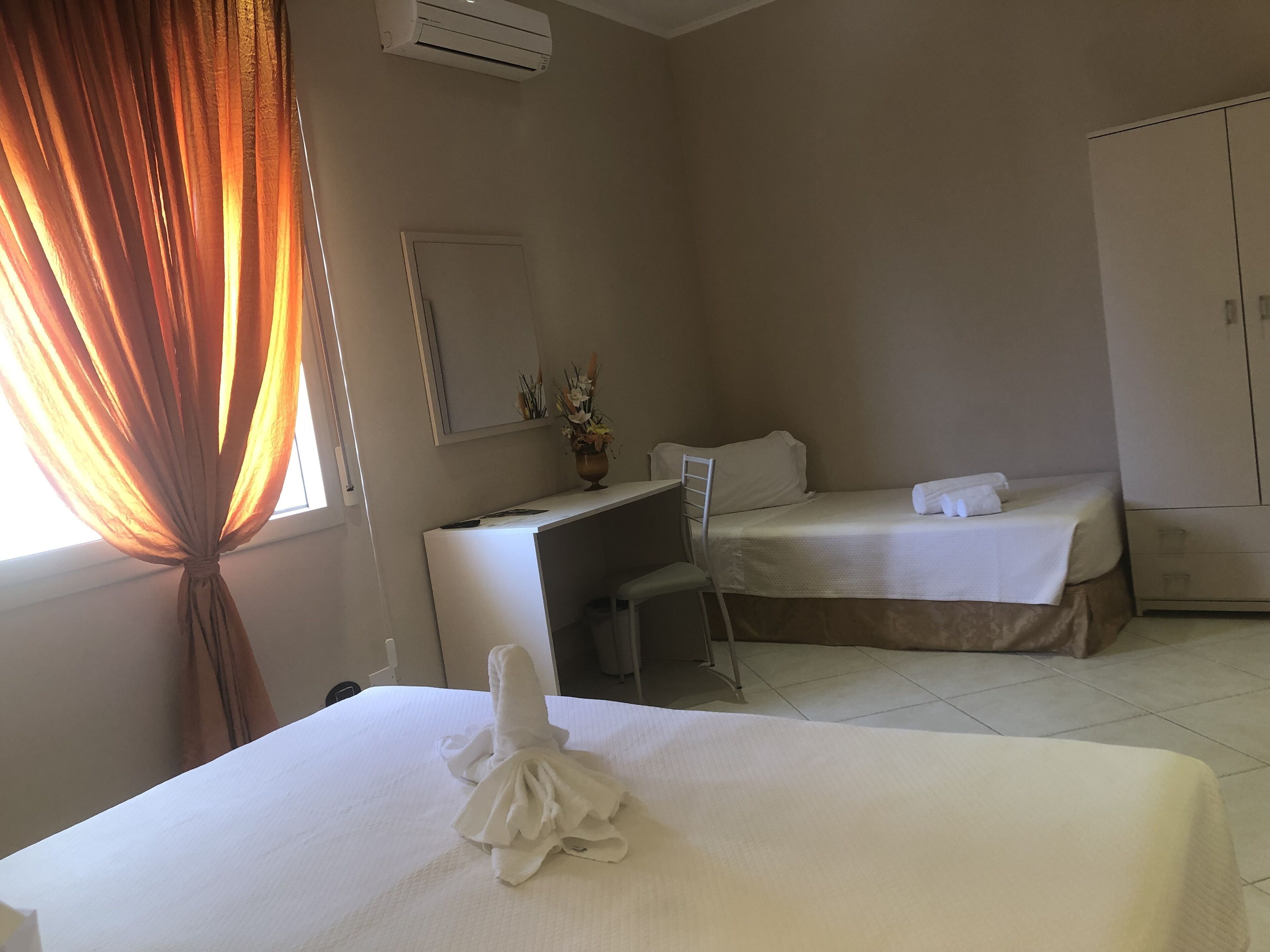 A hotel room with two beds, a desk, a chair, a wardrobe, and a window with curtains.