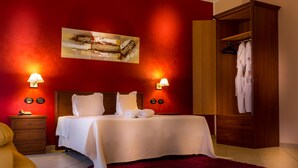 A hotel room with a red wall, a bed with white linens, two wall-mounted lamps, a wooden wardrobe, and a red rug. - B&B Il Tempio di Hera (Castelvetrano)