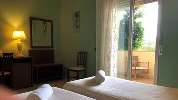 Une chambre d’hôtel avec deux lits, un bureau avec une lampe, une chaise, une petite table, un miroir et un balcon avec une chaise.