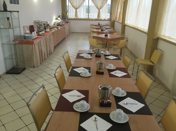 A dining area with multiple tables set for breakfast, including plates, cups, and cutlery.