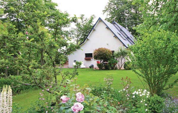 Een wit huis met een schuin dak, omgeven door een verzorgde tuin met verschillende bloeiende planten en een gazon.