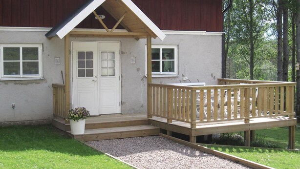 A building with a wooden deck, a white door, and a small garden area. - 2 bedroom amazing home in Hestra (Hestra)