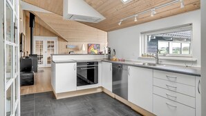 A modern kitchen with a central island, built-in oven, and a large window providing a view. - Beach front home in Fanø with sauna (Fanø)