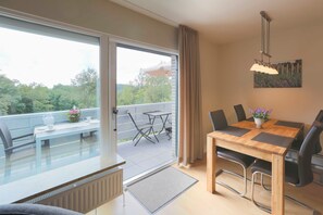 A modern dining area with a wooden table and chairs, a view of the outdoors through a sliding glass door, and a small balcony with a table and chairs.