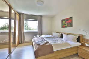 A modern bedroom with a large bed, a bedside table, a nightstand, and a window with curtains.