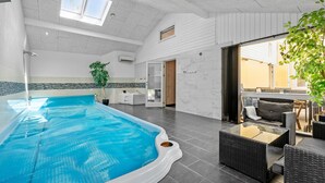 En inomhuspool med glasväggar, ett matområde med möbler i rotting och utsikt över omgivningen.