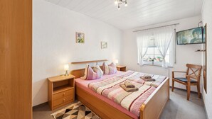 A bedroom with a wooden bed, bedside tables, a TV, and a window with curtains. - Cozy home in Strohn with kitchen (Strohn)
