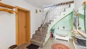 A staircase with a metal railing leading to a landing with a white bench and a mirror with magazines. - Cozy home in Strohn with kitchen (Strohn)