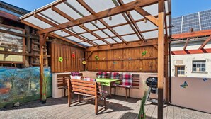 An outdoor seating area with wooden benches and a table, surrounded by a wooden pergola and decorative wall panels. - Cozy home in Strohn with kitchen (Strohn)