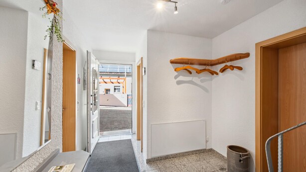 A hallway with a wooden door, a coat rack, a trash can, and a view of buildings outside. - Cozy home in Strohn with kitchen (Strohn)