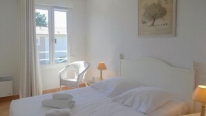 A bedroom with a bed, white curtains, a chair, a lamp, and a framed botanical illustration on the wall. - Awesome home in Montauroux (Montauroux)