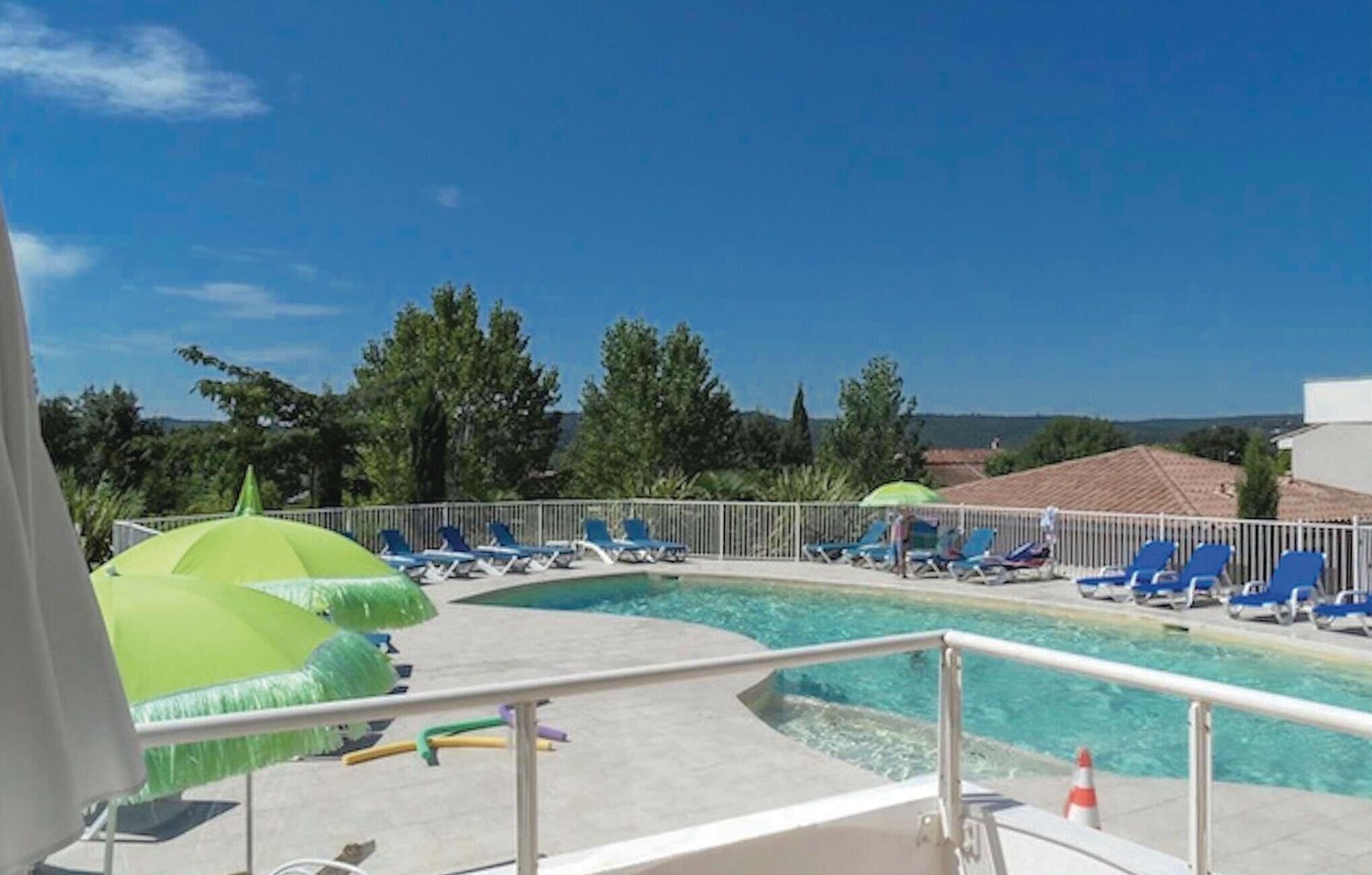 Ett poolområde med blå solstolar och ett grönt parasoll.