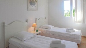 A room with two single beds, white bedding, a nightstand with a lamp, and a window with curtains. - Awesome home in Montauroux (Montauroux)