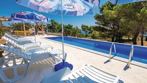A poolside area with lounge chairs and umbrellas, a clear blue pool, and a wooden pergola in the background.
