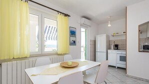 A modern kitchen with white appliances, a dining table with chairs, and a view of the sea through the windows.