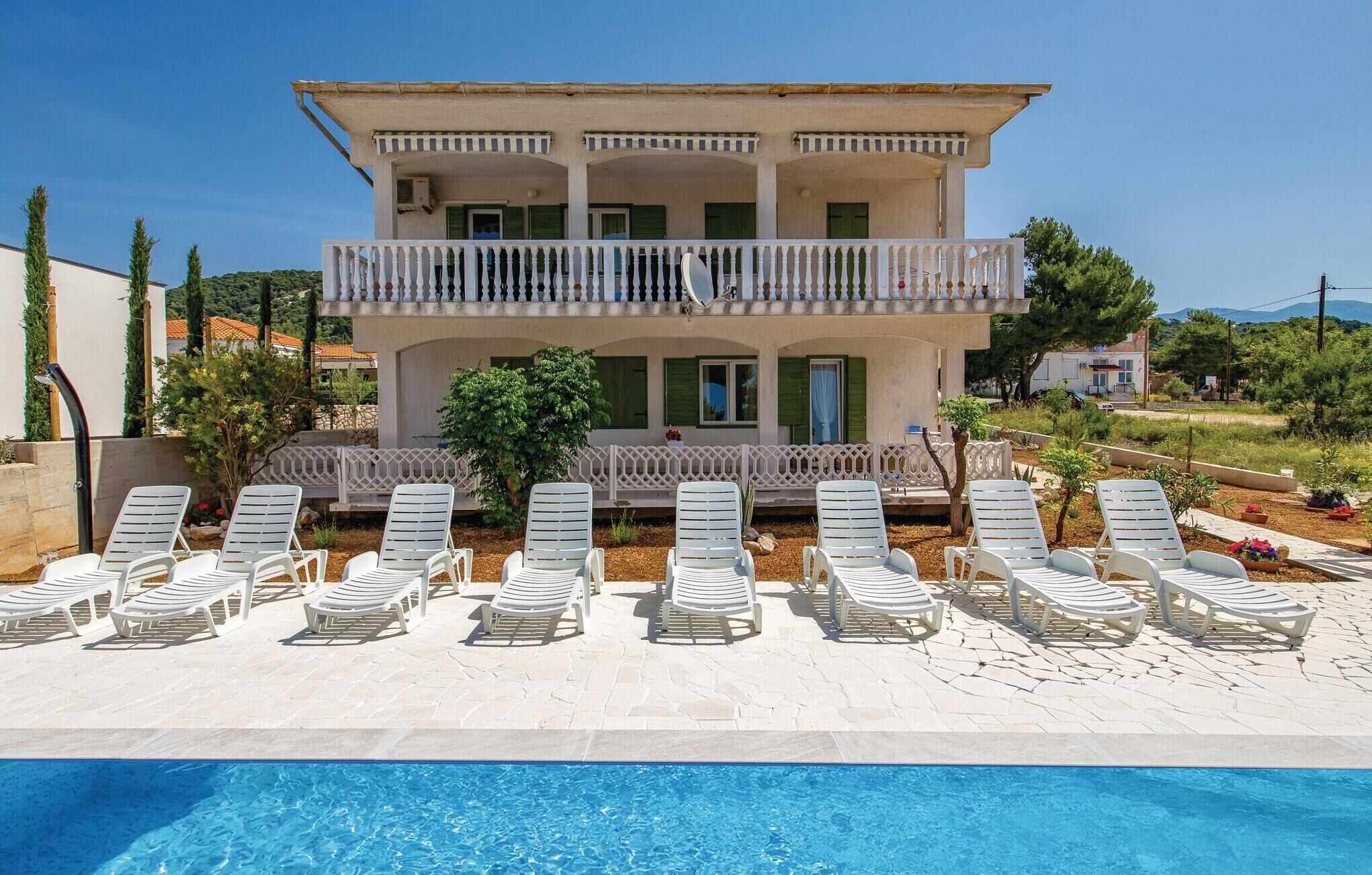 A two-story building with a pool and sun loungers in front.