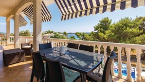 A covered outdoor seating area with a table and chairs, overlooking a scenic view of the sea and greenery.