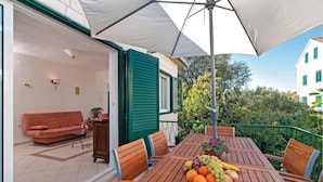Een terras met een eettafel gedekt voor twee personen, een bank en een grote parasol voor de schaduw.