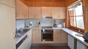 Une cuisine compacte avec des meubles en bois, un four encastré, une plaque de cuisson et une fenêtre avec des rideaux.
