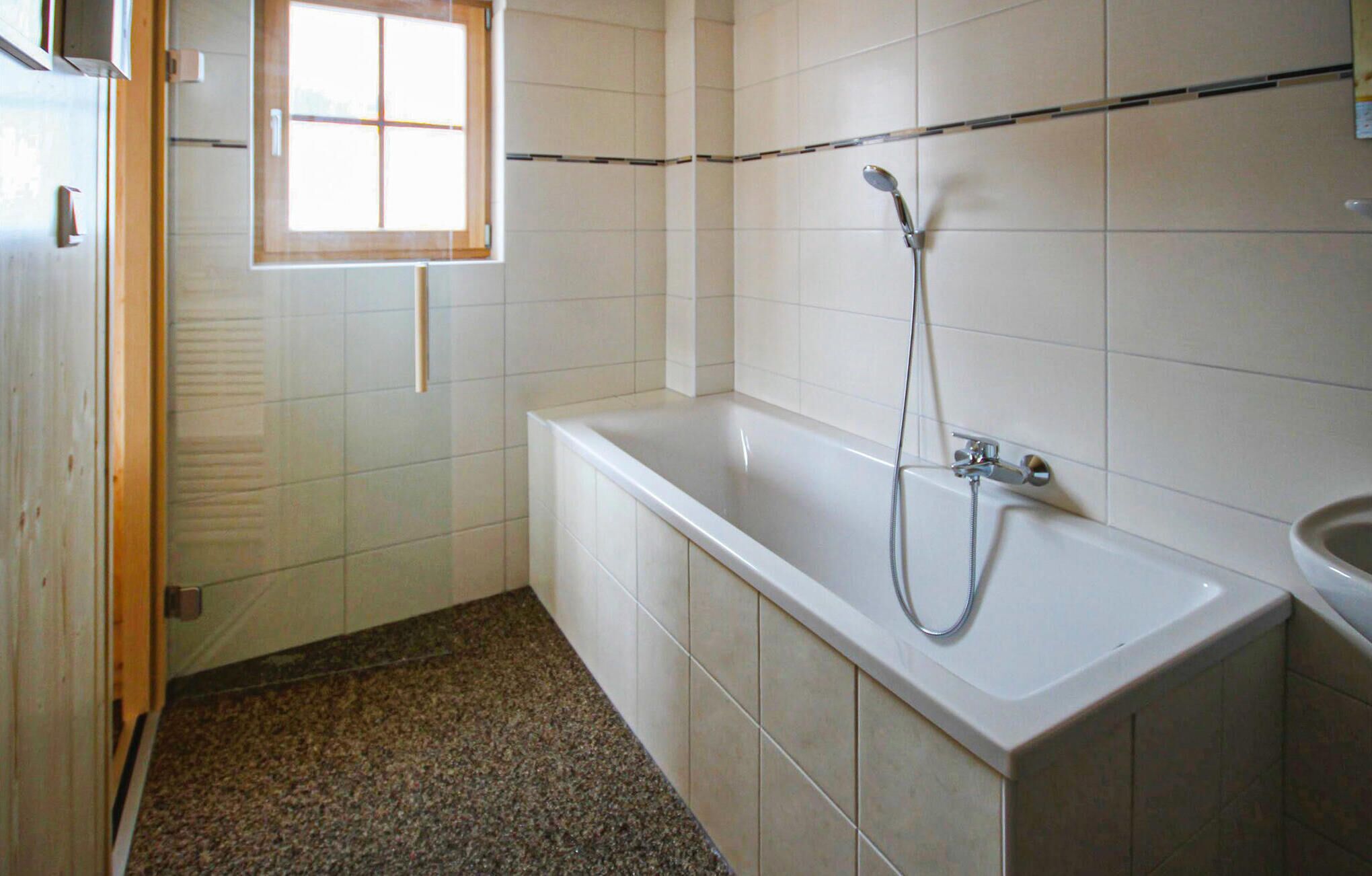 Une salle de bain avec une baignoire blanche, une douche et une fenêtre.