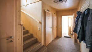 Un intérieur en bois avec un escalier recouvert de moquette, des portes en bois et un porte-manteau avec des vestes.
