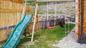 Une structure de jeu en bois avec un toboggan vert et une balançoire rouge.