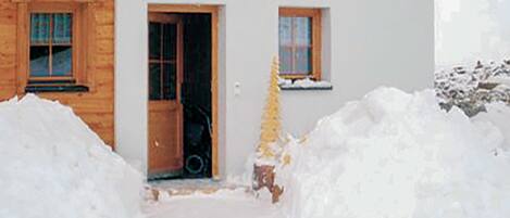 A wooden cabin with a door and a window, surrounded by snow.