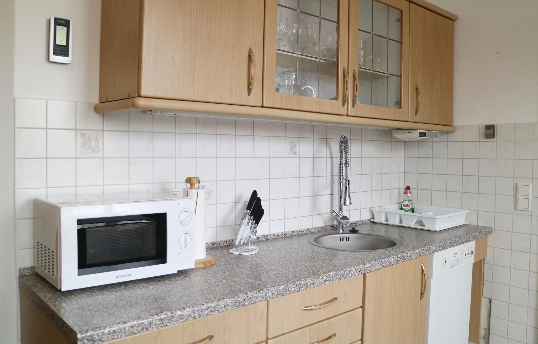 Une cuisine avec des meubles de rangement en bois, un micro-ondes blanc, un évier et une bouteille de liquide vaisselle.