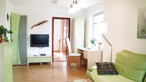 A living room with a green sofa, a TV, a desk, and a chair. There is a door leading to another room. - 1 bedroom nice apartment in Börgerende (Börgerende)