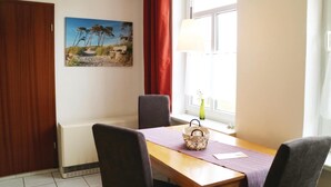A dining area with a wooden table, four chairs, a painting of a beach scene, a red curtain, and a window with a lamp. - 1 bedroom nice apartment in Börgerende (Börgerende)