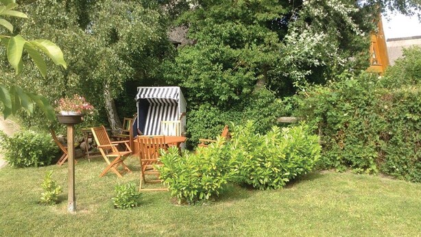 A garden with a wooden table and chairs, a striped canopy, and various plants. - 1 bedroom nice apartment in Börgerende (Börgerende)