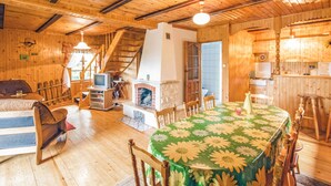 A cozy wooden cabin interior with a fireplace, a dining table with a floral tablecloth, and a television in the corner. - 3 bedroom cozy home in Dabrówno (Dabrówno)