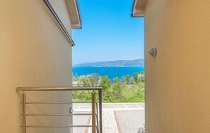 A view from a balcony with a metal railing, overlooking a road and a coastal landscape with a clear blue sky. - Lovely apartment in Labin with WiFi (Labin)