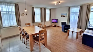 Een woonkamer met een houten eettafel, stoelen, een televisie en een bank.