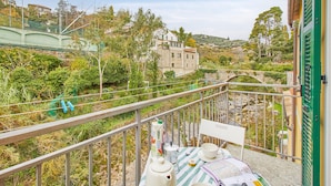 A balcony with a table set for tea, overlooking a stone bridge and lush greenery.