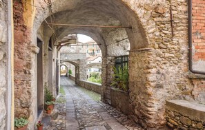 Une ruelle étroite en pierre, bordée d’arcades, agrémentée de plantes en pot et dotée d’un chemin pavé.