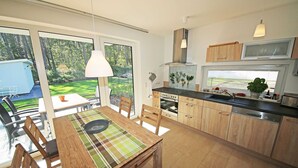 A modern kitchen with wooden cabinets, a dining table with chairs, and a large window overlooking a garden. - Vacation home Igelbau Whg. 01 with terrace - MR: Holiday home Igelbau with 2 (Baabe)