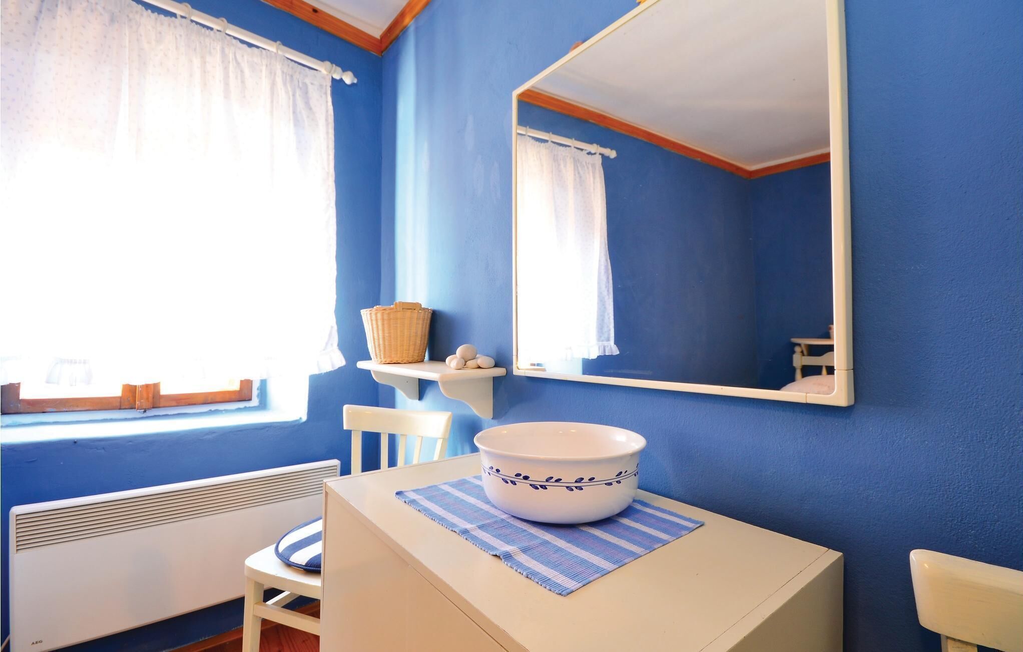 A bathroom with blue walls, a white sink, a mirror, and a window with white curtains.