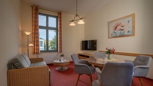 A furnished living room with a sofa, chairs, a dining table, and a TV.